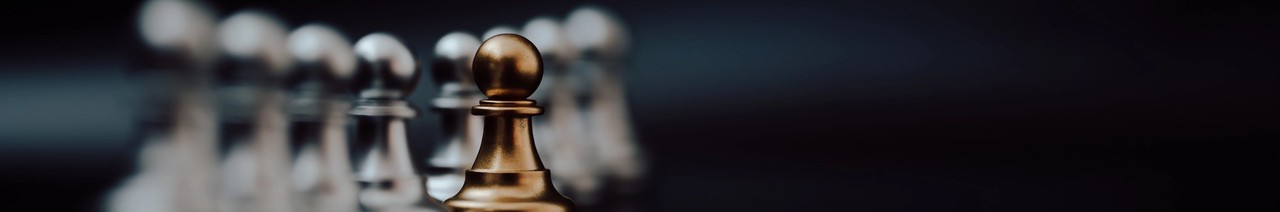 Tumma shakkilauta, jossa kultainen shakkinappula erottuu hopeisten shakkinappuloiden rivistä